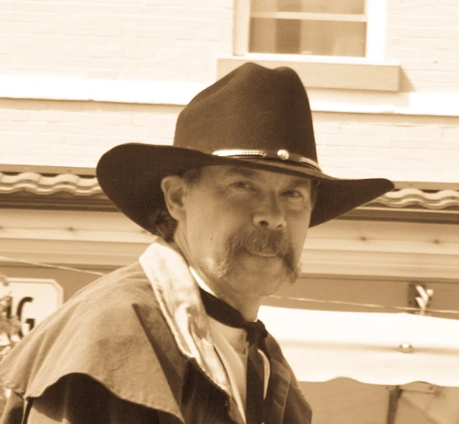 man wearing a black hat and jacket next to a white building