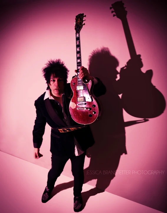 man in suit and black tie posing with pink guitar