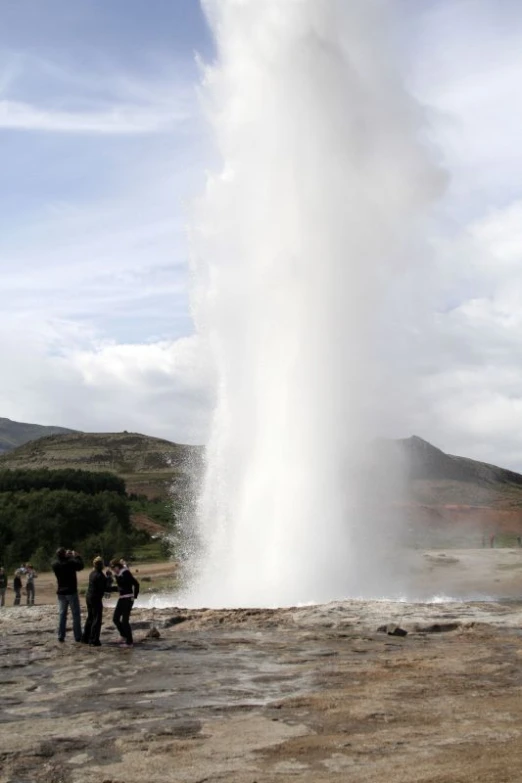 a geyser erupting water into the air as several people gather around to watch