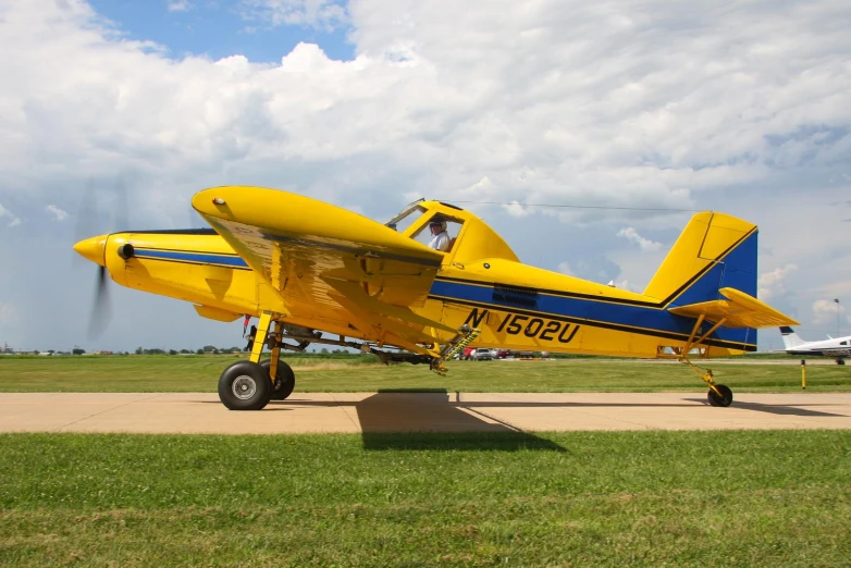 a yellow plane parked in a grassy field with an airplane on the ground