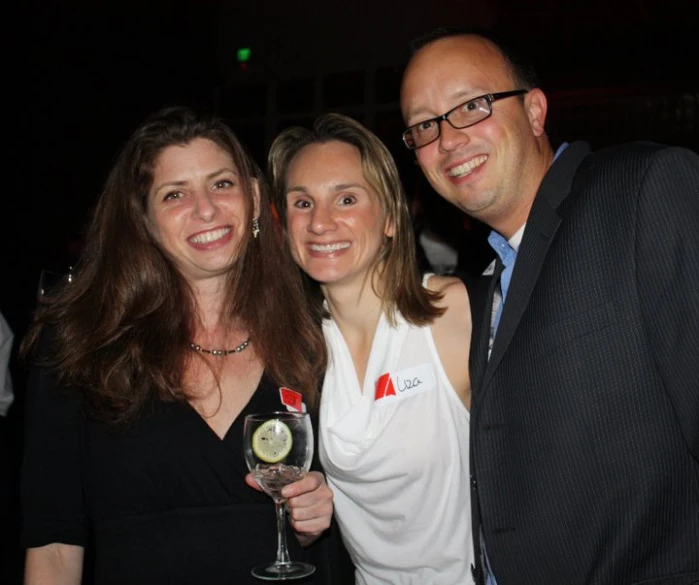 three people smile at the camera holding up glasses