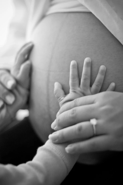 the hands are in the pregnant belly while the other hand is holding the baby