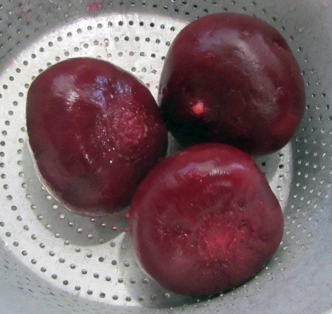 three plums are in a silver bowl on the table