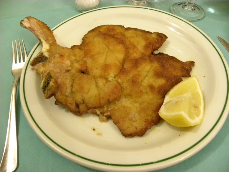 the plate has some fried meat with a side of lemon wedges