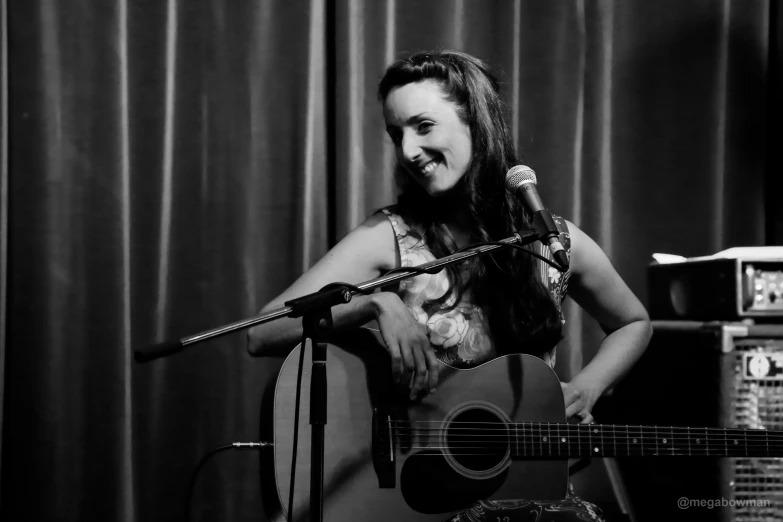 a woman with a guitar and microphone stands next to a sound booth