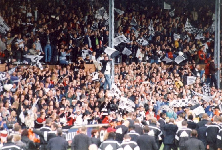 a large crowd of fans sitting on the sidelines at a soccer game