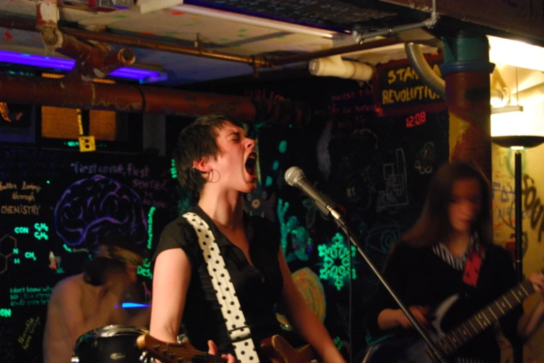 a woman singing into a microphone with two guitars