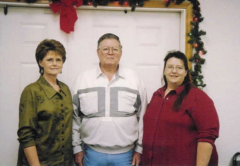 an older man and two younger women standing in front of a christmas wreath