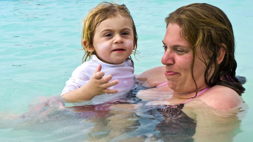 the woman holds a baby as she is swimming in the pool