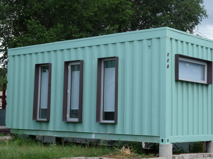 a small green house with brown windows sitting in a grass field