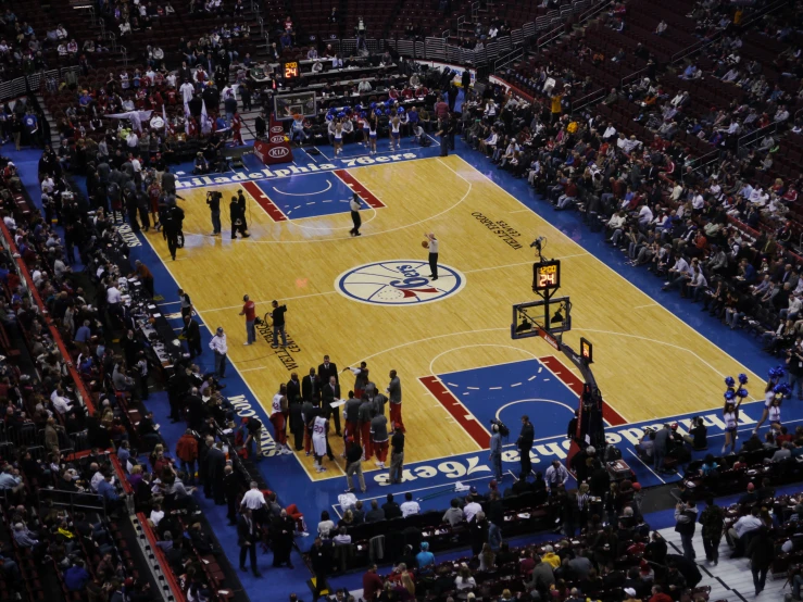 a crowd of people stand on the floor of a basketball court