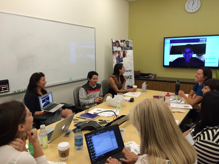 a group of people sitting at a conference table watching a computer