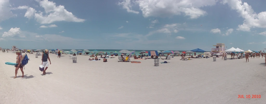 a beach full of people and umbrellas on a cloudy day