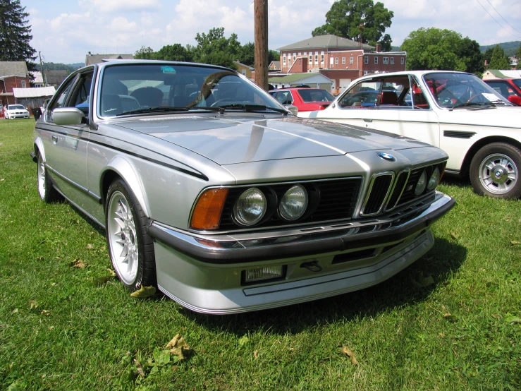 an old bmw is sitting in the grass next to two other cars