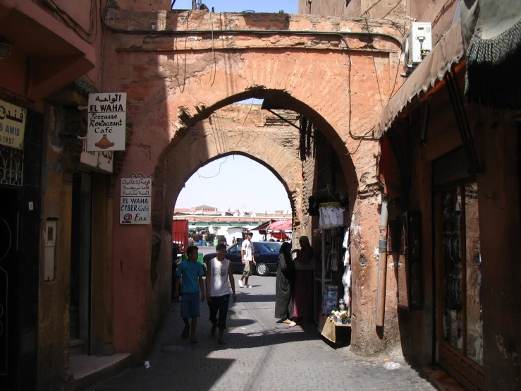 people walking down a narrow street under a stone arch