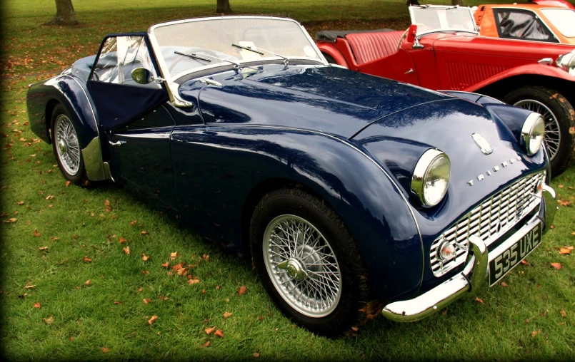 two vintage cars parked next to each other on a lush green field