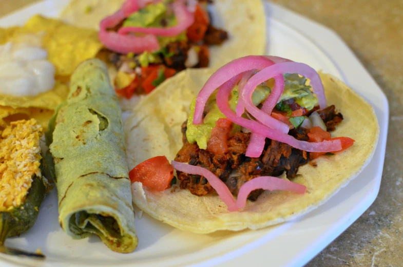 several tacos sit on a white plate on a table