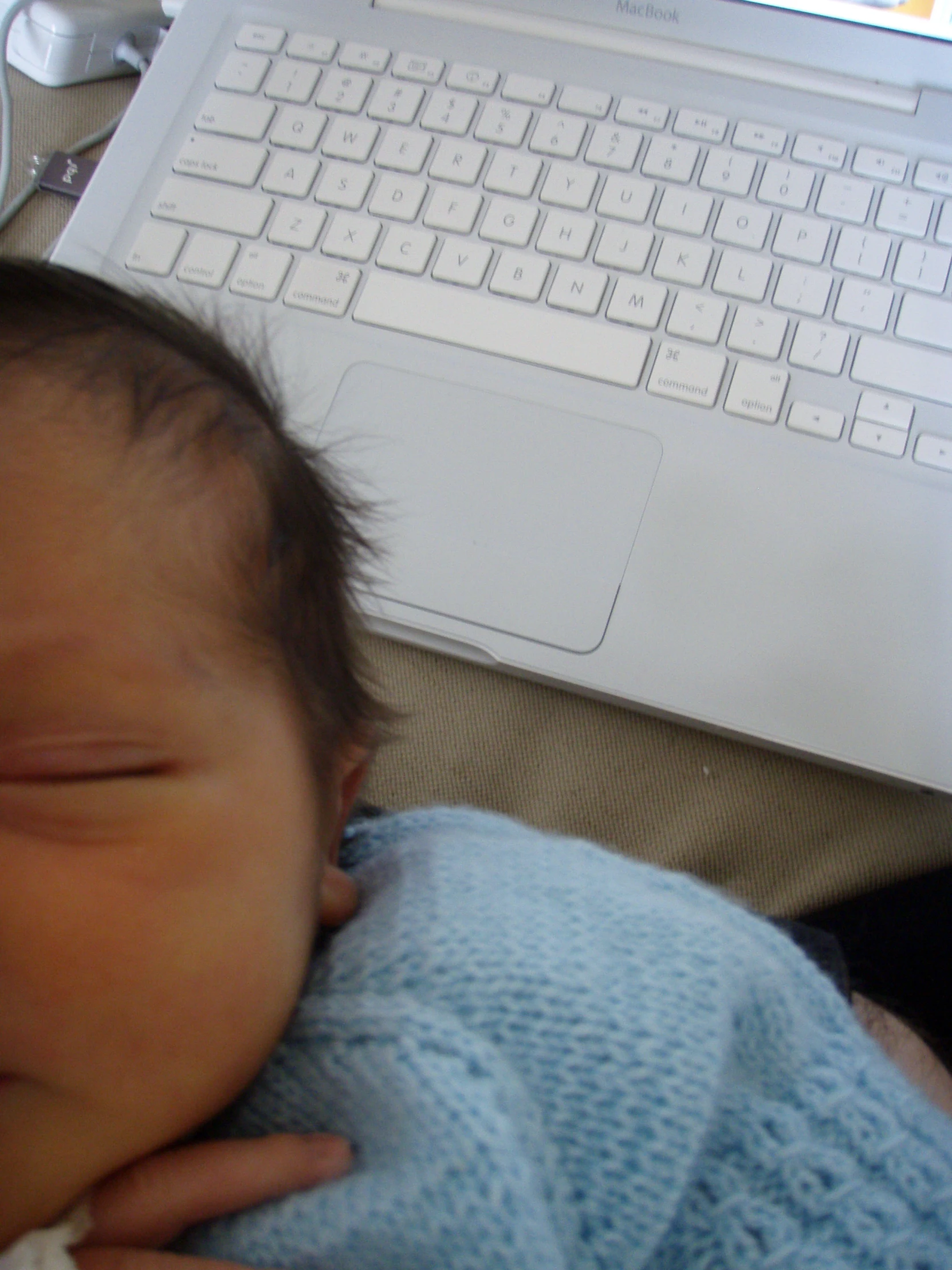 an infant laying next to a laptop computer