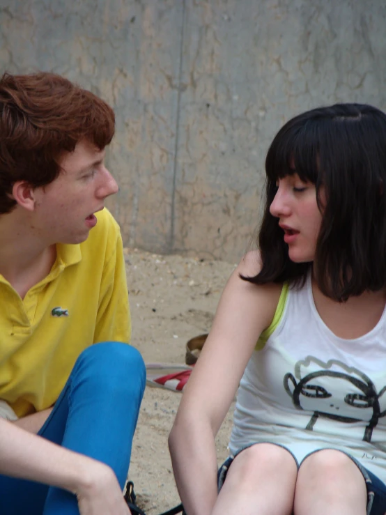 two young people sitting in the sand outside