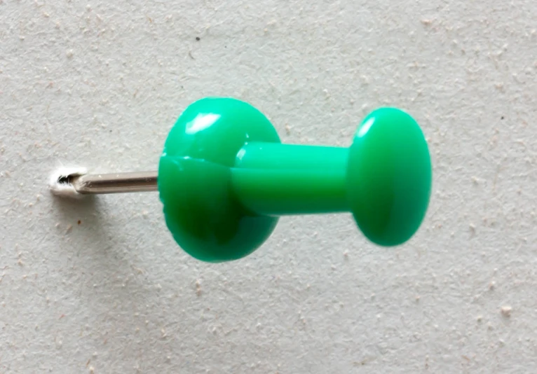 a green plastic object is sitting against a white wall