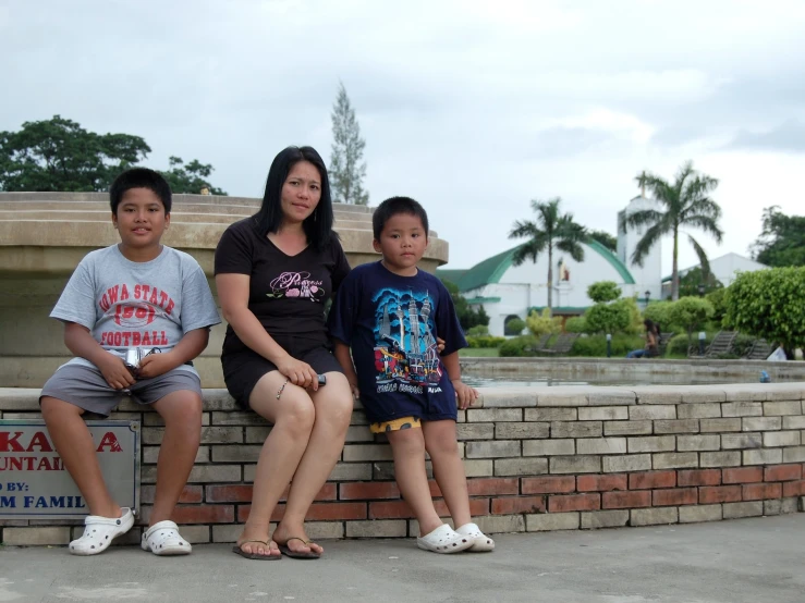 three people sitting on top of a brick wall