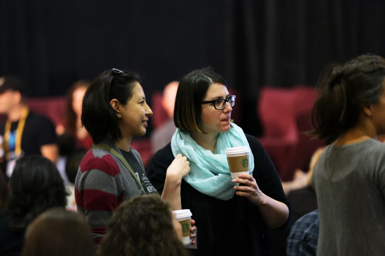 two women sharing drinks while standing in an auditorium