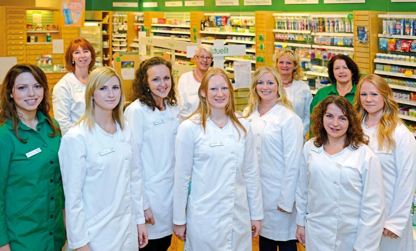 a group of women wearing white lab coats stand in a pharmacy