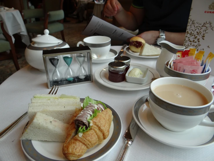 a plate with sandwich, cup of tea and a tea pot