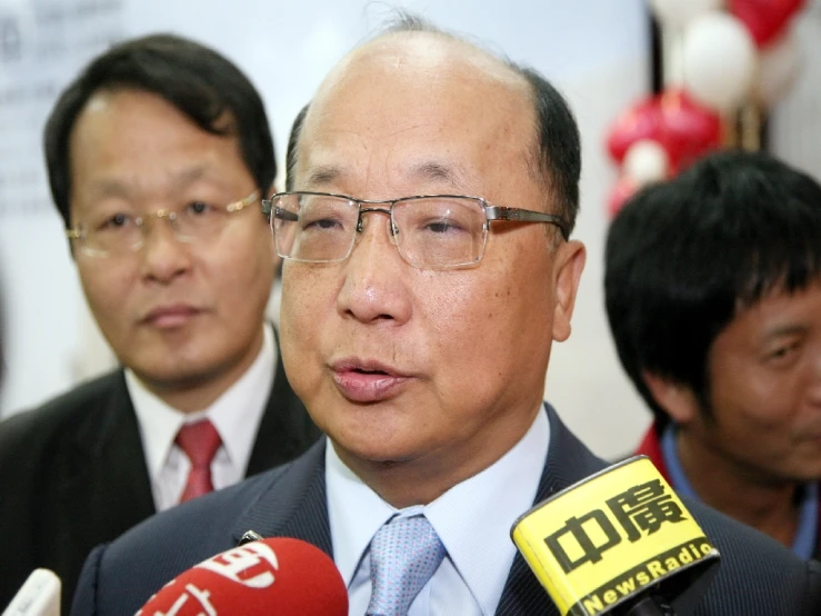 an asian man wearing glasses and a tie speaking to a camera