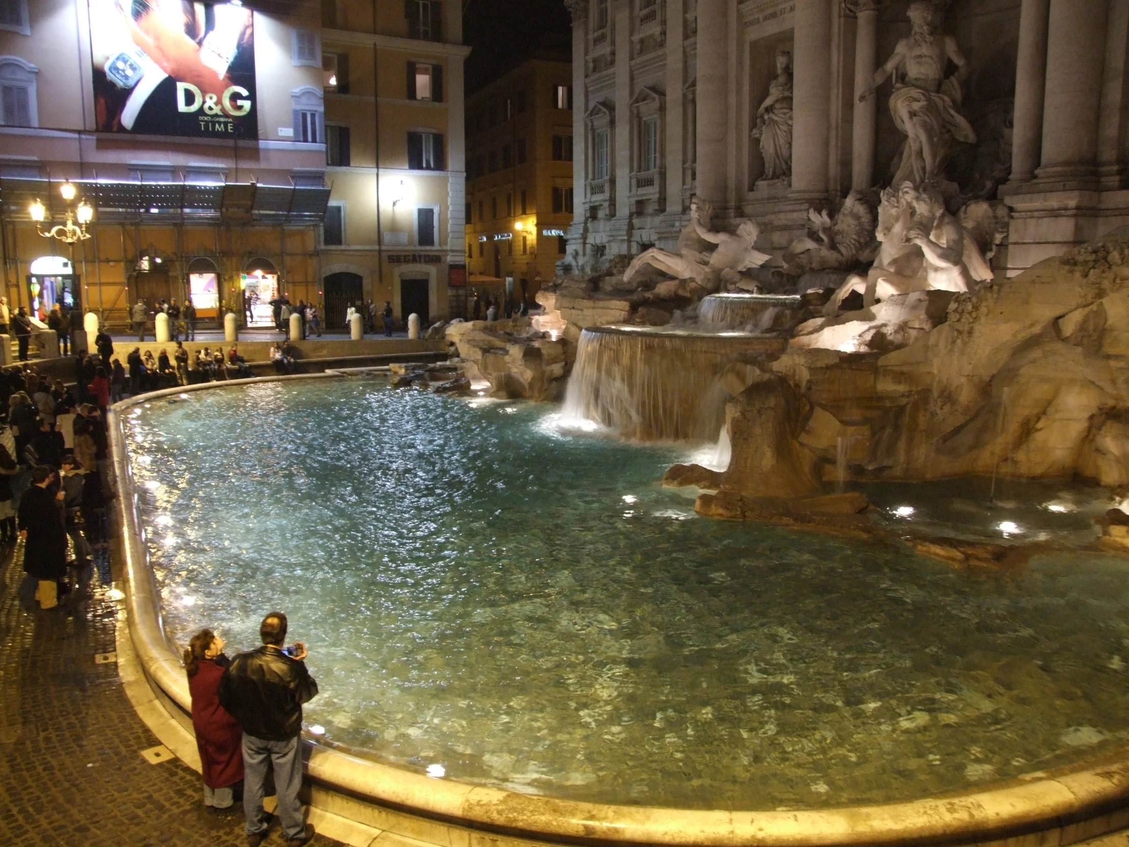 people are standing by a fountain at night