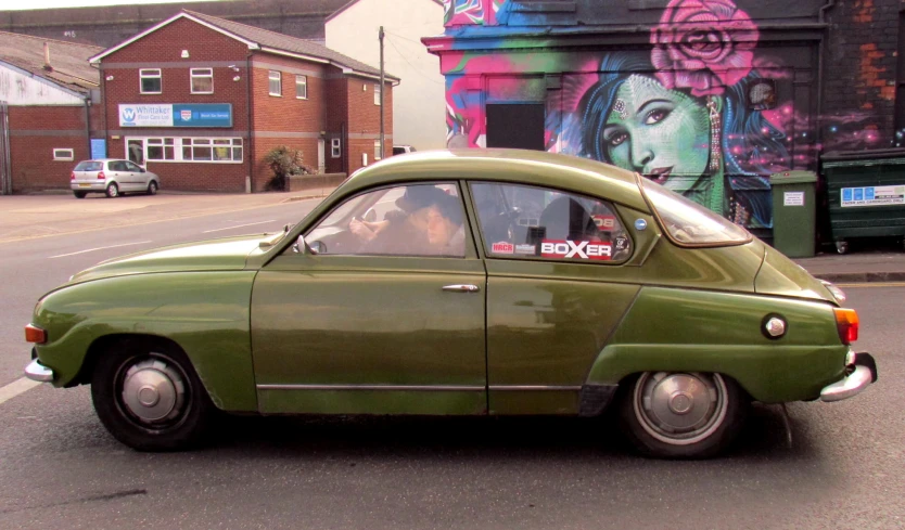 a small green car in front of colorful graffiti on a wall