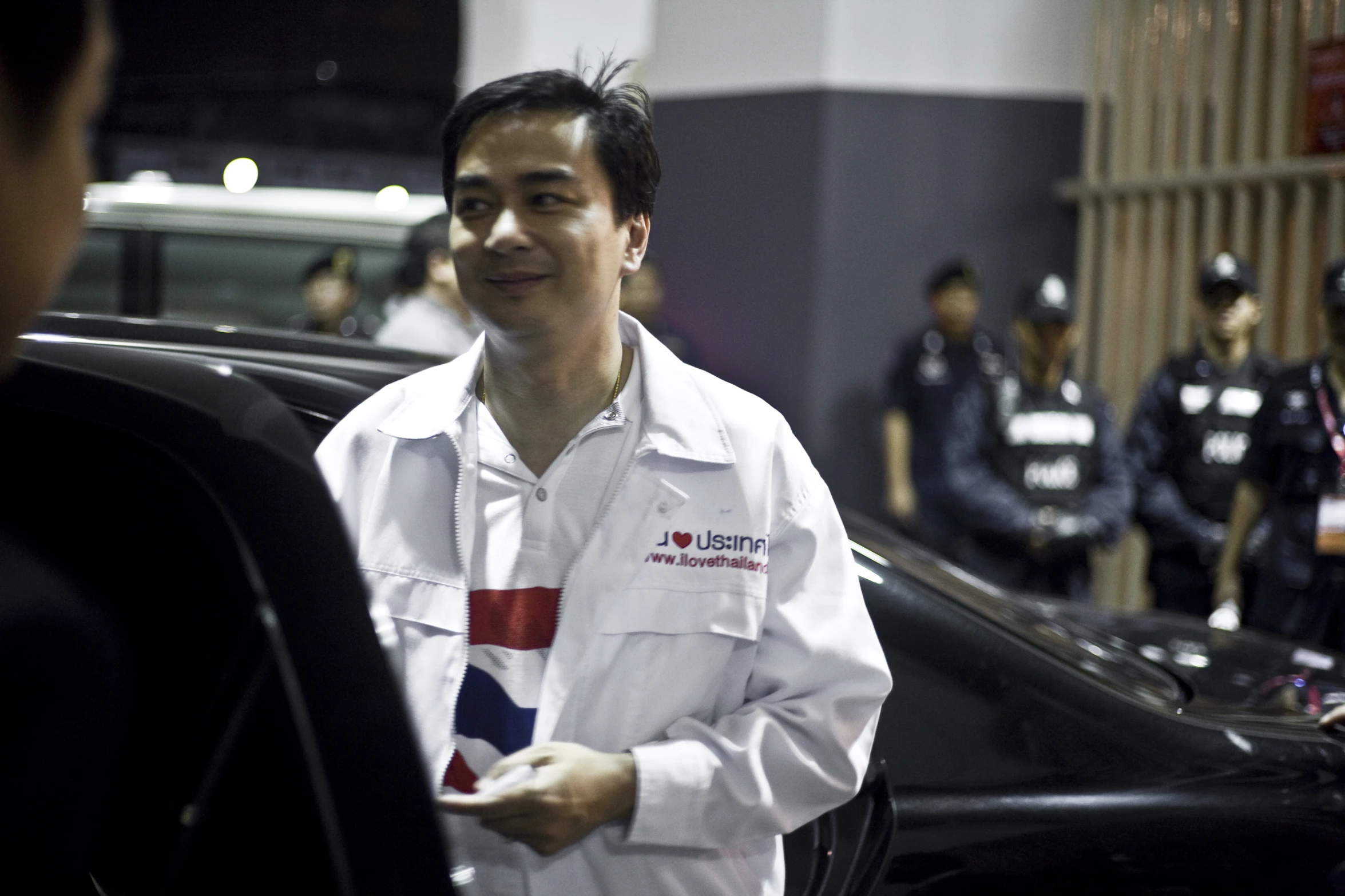 two men talking next to a car at an auto show