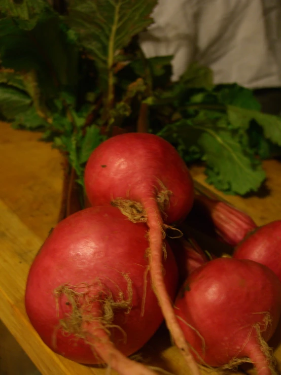 some radishes are on a wooden table with green leaves