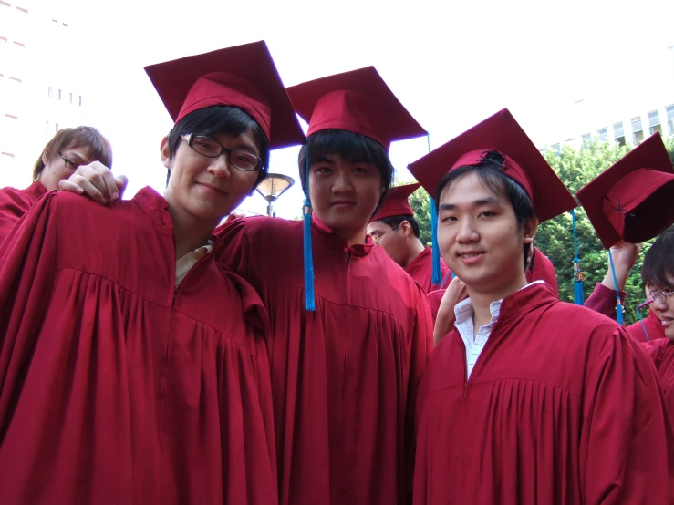 four students are standing in graduation gowns and holding their hats