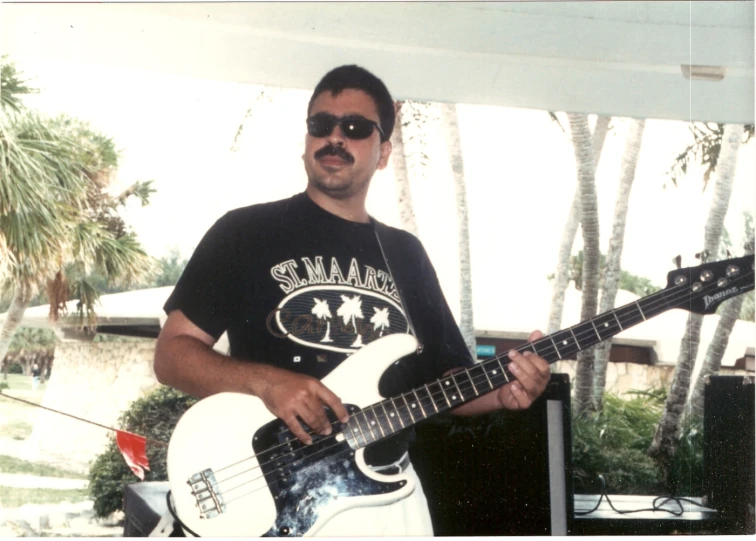 a man holding a white guitar standing in front of palm trees