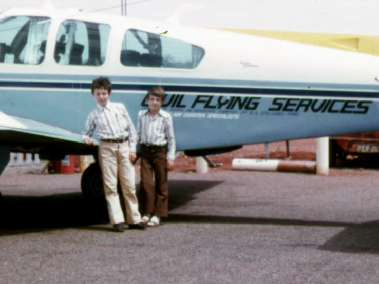 two boys standing next to an airplane on a tarmac