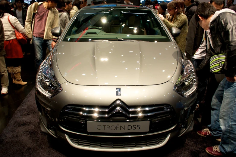 people are gathered around and looking at a silver car