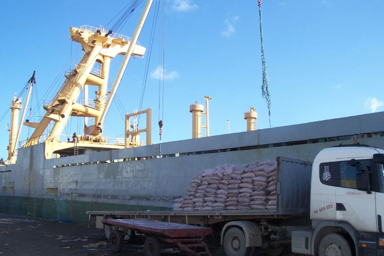 a truck carrying two large cargo bags next to a large crane