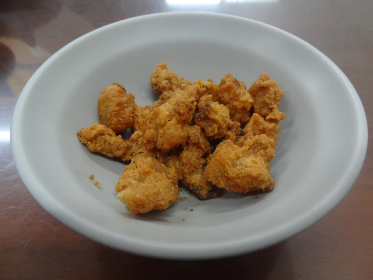 a white bowl containing fried food is sitting on a wooden table