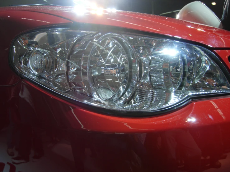 a close up po of a red car with the headlights shining
