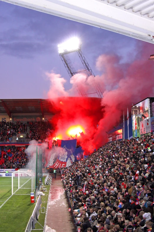 soccer fans in the stands, some holding red smoke