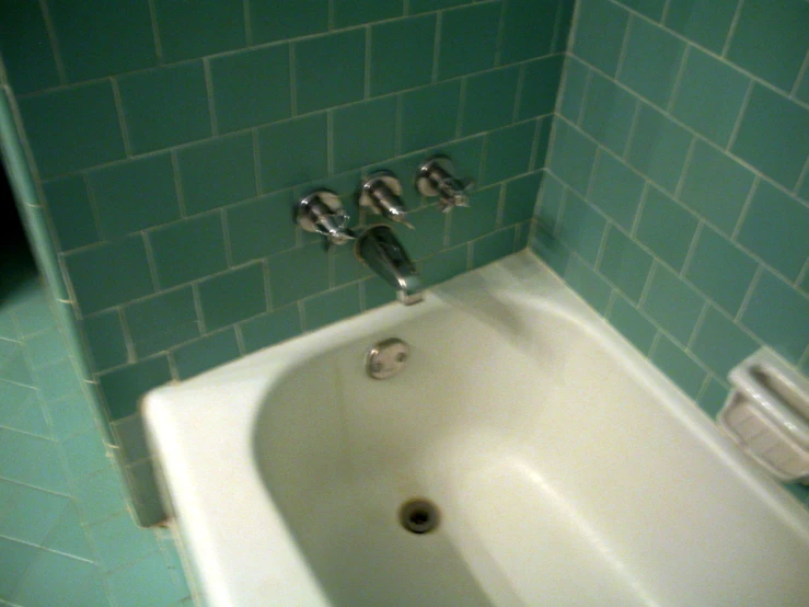 the bathtub has two faucets and green tile