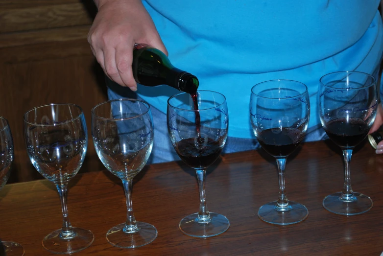 a person pours wine into several wine glasses