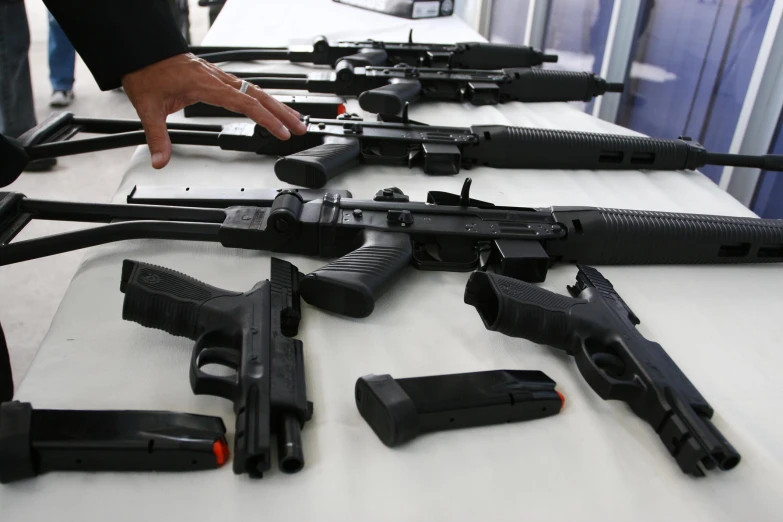 a person pointing to guns lined up on a table