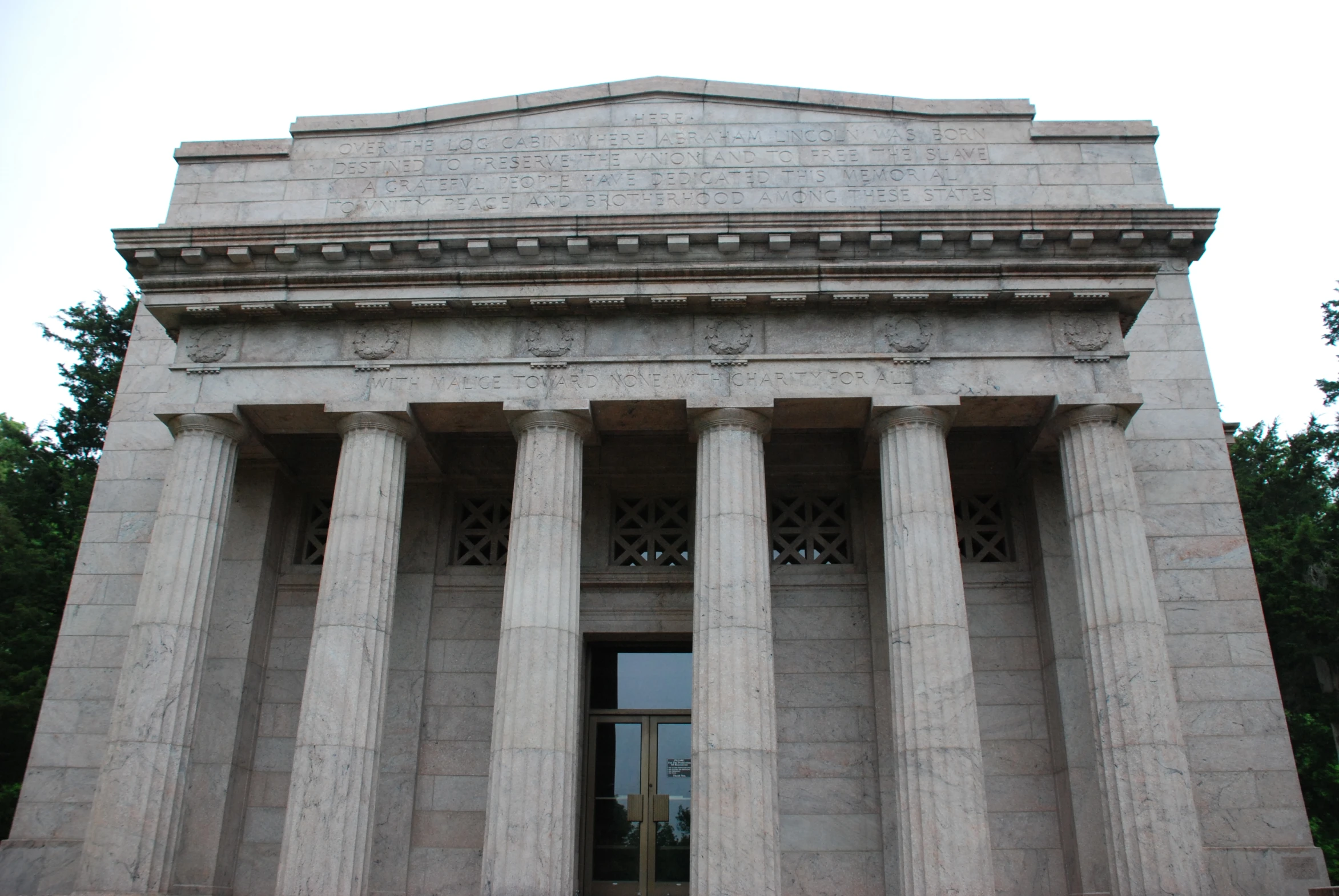 a building with a door and three pillars next to trees