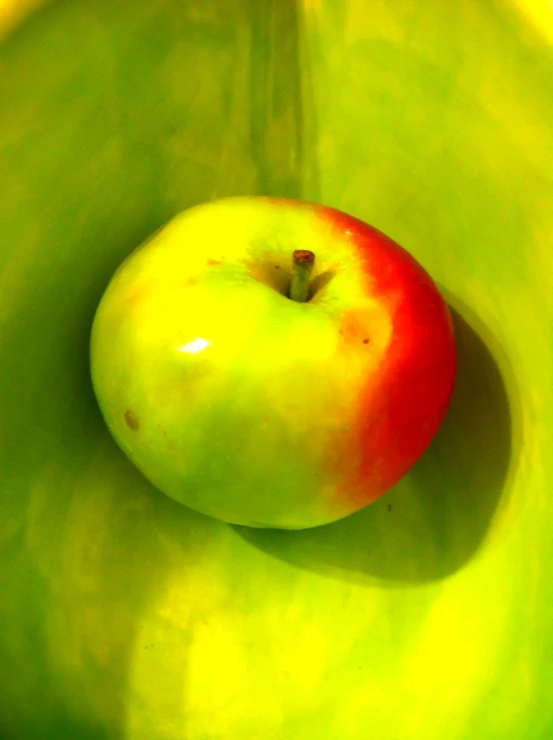 an apple sitting in a circular bowl filled with green apples