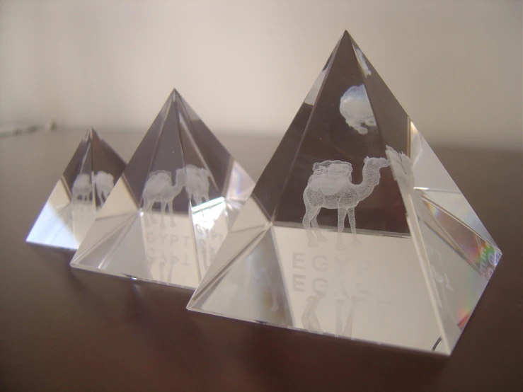 three decorative glass pyramids sitting on top of a wooden table