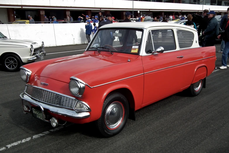 a classic car on display in a parking lot with people standing and standing around