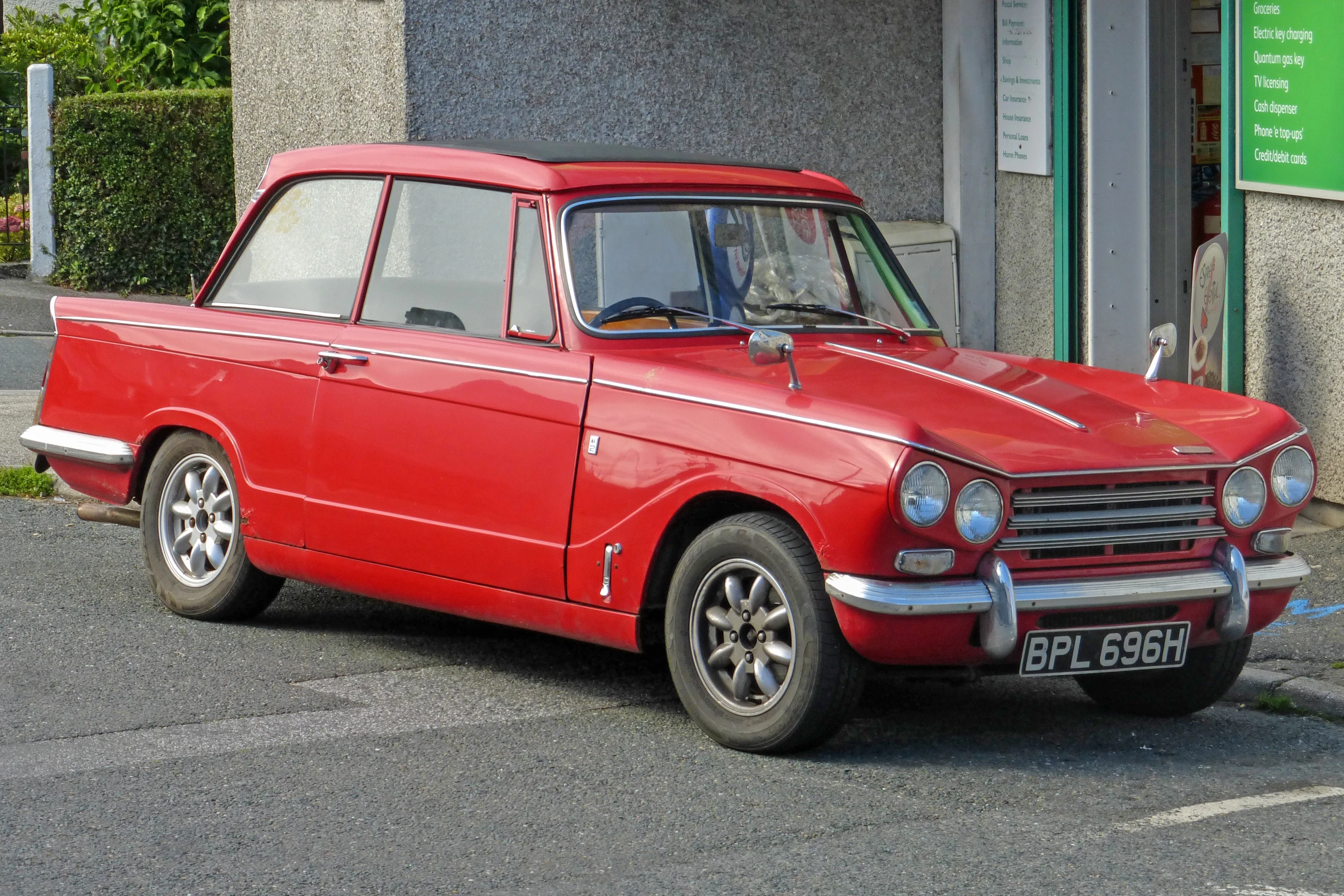 a red car parked in a street next to a sign