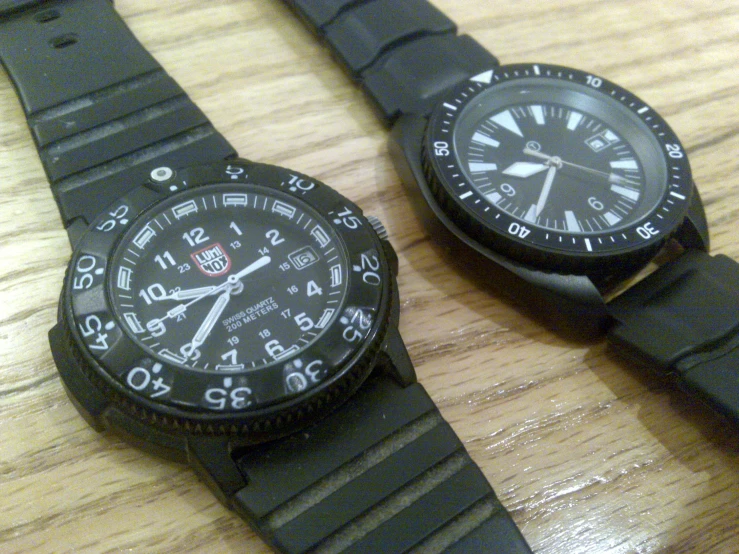 two watches are sitting next to each other on the wooden table